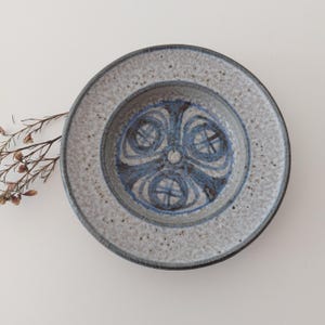 May include: A white ceramic bowl with a blue and gray geometric design. The bowl has a speckled glaze and a slightly raised rim.