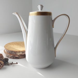 May include: White ceramic coffee pot with a gold trim around the lid and handle. The pot has a tall, slender shape.
