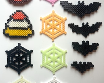 May include: A collection of Halloween-themed perler bead crafts, including pumpkins, bats, and spiderwebs in various colors, such as black, orange, pink, white, and green.