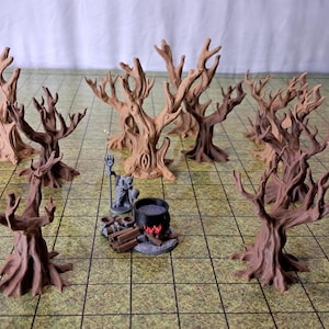May include: A collection of ten brown, leafless, gnarled tree miniatures arranged in a circle on a green grid mat. In the center, a small gray figure stands next to a black cauldron placed over a pile of brown logs with painted red flames.