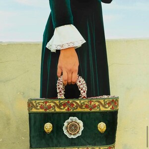 May include: A green velvet handbag with gold trim and lion head embellishments. The bag features a white lace detail and a beaded handle.