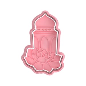 Può includere: Un tagliabiscotti rosa a forma di edificio stilizzato con cupola e finestre ad arco, posto sopra un fiore di loto. Il tagliabiscotti ha un design a strati con un contorno bianco, creando un effetto 3D. Il design è simmetrico.