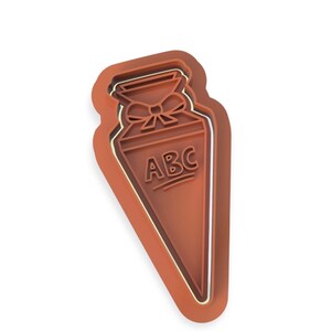 Könnte beinhalten: Brauner Ausstecher in Form einer Schultasche mit Schleife oben und den Buchstaben "ABC". Der Ausstecher hat eine weiße Kontur. Ideal für Kekse.