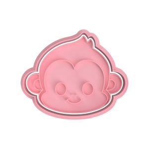 May include: A pink monkey-shaped cookie cutter with a smiling face, large eyes, and rounded ears. The cutter has a white outline and is designed for baking. The overall design is simple and cute.