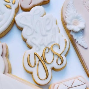 Può includere: Biscotto bianco con la scritta "She said yes" in lettere dorate.