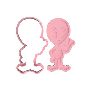 May include: Pink plastic cookie cutter in the shape of an alien with a peace sign. The cutter is shown with a separate outline for cutting out the shape.