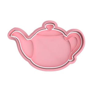 Op de afbeelding: Een roze theepotvormige koekjesuitsteker met een witte omtrek. De uitsteker heeft een tuit, handvat en deksel en is ontworpen voor het maken van traktaties met een theefeestthema. Het ontwerp is eenvoudig en strak, perfect voor bakliefhebbers.