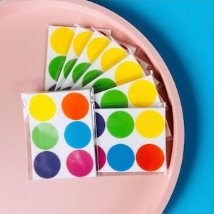 Op de afbeelding: Een set ronde, kleurrijke stickers in verschillende kleuren, waaronder rood, oranje, geel, groen, blauw en paars. De stickers zijn gerangschikt in een rasterpatroon op een witte achtergrond.