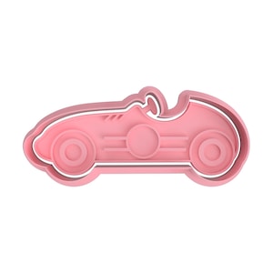 Könnte beinhalten: Ein rosa Ausstecher in Form eines Oldtimer-Rennwagens. Der Ausstecher hat ein detailliertes Design mit Rädern, einem Cockpit und einer stromlinienförmigen Karosserie. Der Ausstecher ist aus Kunststoff und eignet sich zum Herstellen von Keksen oder anderen Leckereien.
