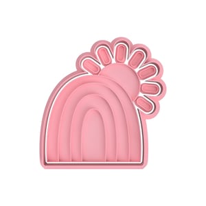 Peut inclure: Emporte-pièce en plastique rose en forme d'arc-en-ciel avec un soleil sur le dessus. Le soleil a un design simple avec des rayons.
