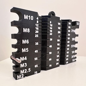 Op de afbeelding: Een zwart plastic gereedschap met meerdere sleuven om verschillende schroefmaten te meten. Het gereedschap is gemarkeerd voor metrische maten M2, M2.5, M3, M4, M5, M6, M8 en M10, evenals imperiale maten 1/8, 3/16, 5/16, 3/8, 7/16, 1/4, 1/2, 3/4, 1, 1 1/4, 1 1/2, 1 3/4, 2 en 2 1/4 inch.