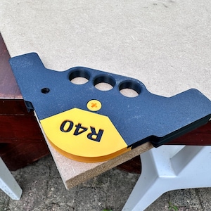 Op de afbeelding: Een zwarte en gele hoekklem met de tekst "R40" erop gedrukt. De klem heeft vier vingergaten en is gemaakt van plastic.