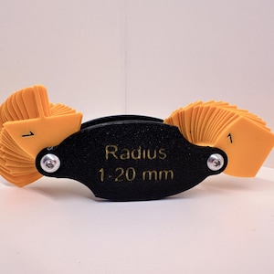 Könnte beinhalten: Ein schwarzer und orangefarbener Radiuslehre mit einem Bereich von 1-20 mm. Die Lehre verfügt über eine Reihe von orangefarbenen Kunststofflaschen, mit denen der Radius einer Kurve gemessen werden kann.