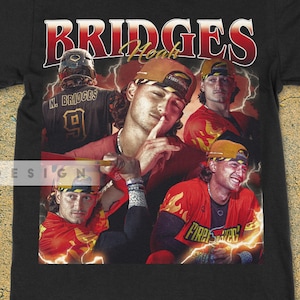 May include: Black t-shirt featuring a collage of images with the text "BRIDGES" in red and white. The images show a person wearing a baseball cap and jersey. The shirt has a vintage, retro design.