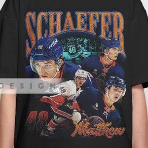 May include: Black t-shirt featuring a vintage-style graphic of a hockey player in a blue uniform. The design includes the name "SCHAEFER" in orange lettering and the number "48" with the name "Matthew". The shirt is a casual wear item.