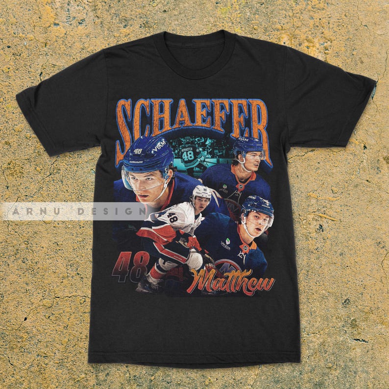 May include: Black t-shirt featuring a vintage-style graphic of a hockey player with the name "Schaeffer" in orange lettering. The design includes the number "48" and the name "Matthew" in a script font.