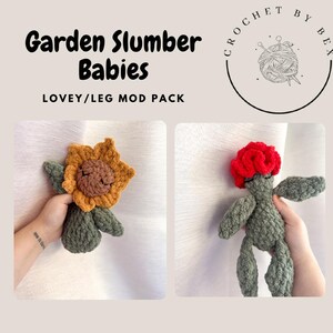 May include: Two handmade crochet baby toys. One is a sunflower with a smiling face, the other is a figure with a red flower head. The text reads "Garden Slumber Babies" and "LOVEY/LEG MOD PACK". The toys have a soft, textured appearance.