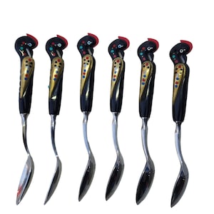 May include: Six decorative spoons with black handles featuring a bird design with red crests, gold accents, and colorful dot patterns. The spoons have a curved, silver-colored bowl and stem, ideal for serving or display.