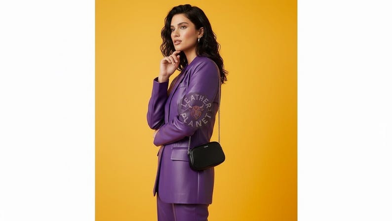 May include: A woman in a purple leather suit and a black crossbody bag. The suit includes a blazer and pants. The bag has a chain strap. The background is a solid yellow color. The Leather Planet logo is visible on the blazer.