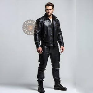 May include: A black leather jacket with a zipper closure and a button-up front. The jacket has a stand-up collar and two pockets on the front. The model is wearing black leather pants with a zipper detail on the front.