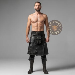 May include: A black leather kilt with a matching belt and pouch. The kilt features layered panels and decorative stitching. The model is wearing black boots. The Leather Planet logo is visible in the background.