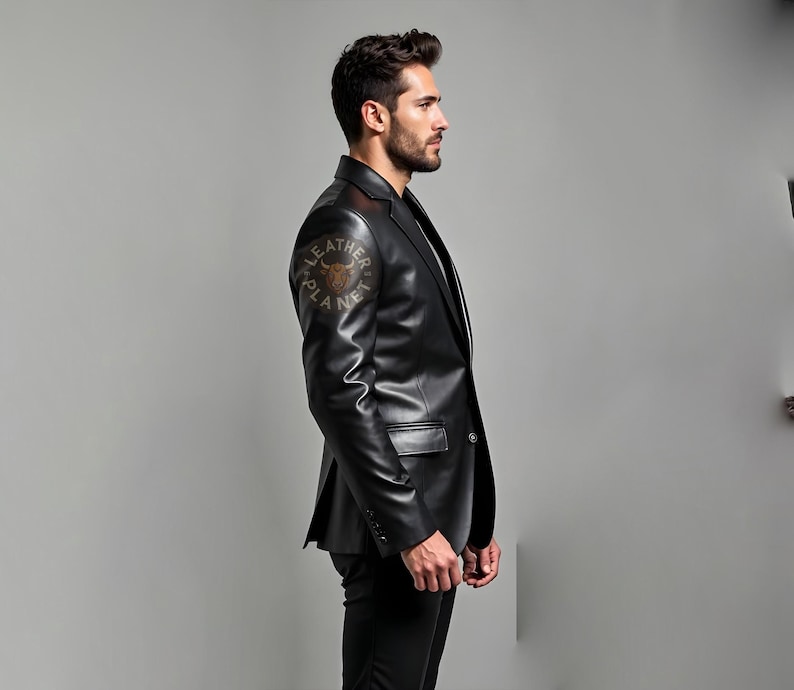 Pu&ograve; includere: Un blazer in pelle nera con revers a lancia e chiusura a un bottone. Il blazer ha un design classico con una vestibilit&agrave; su misura. La manica sinistra presenta un logo circolare con la scritta "LEATHER PLANET". Il modello indossa pantaloni neri.