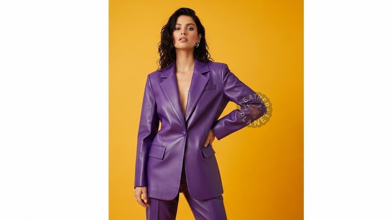 May include: A vibrant purple blazer and matching pants set. The blazer features a classic notched lapel, a single-button closure, and two front pockets. The outfit is made of a smooth, leather-like material, creating a sleek and modern look. The background is a solid yellow.