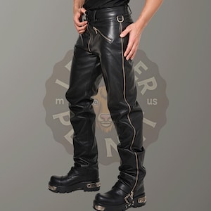 May include: Black leather pants with a zipper detail down the side seams. The pants have a silver buckle belt and are worn with black boots.