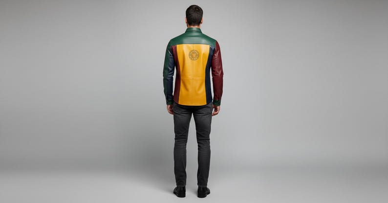 May include: A multi-colored leather shirt with a green, yellow, and burgundy design. The back of the shirt features a circular emblem. The model is wearing dark gray jeans and black shoes. The shirt is a unique fashion statement.