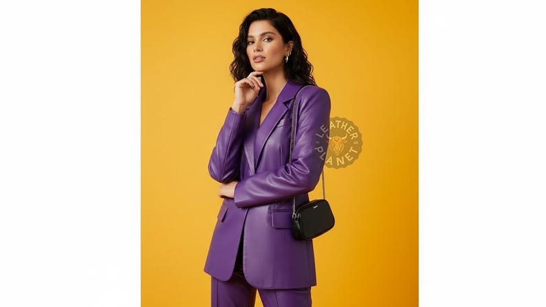 May include: A woman wearing a purple leather blazer and matching pants, paired with a small black purse. The outfit is set against a yellow background. The Leather Planet logo is visible.
