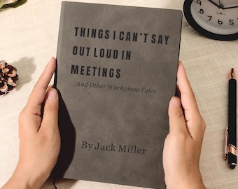 May include: A gray journal titled "THINGS I CAN'T SAY OUT LOUD IN MEETINGS" is held open. A black alarm clock, a pen, and decorative items are also visible. The journal's author is Jack Miller.