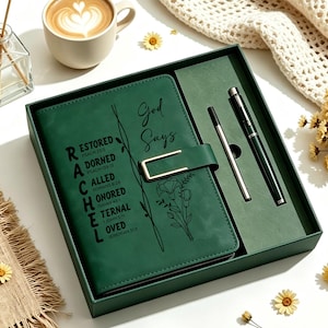 May include: A dark green journal set in a matching box, featuring a gold-tone metal clasp. The journal cover is printed with the text God Says and the name RACHEL, with scripture references. A matching dark green pen is included in the box set.