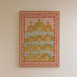 Op de afbeelding: Een badkamerinterieur met een ingelijst kunstwerk met een kleurrijk, abstract ontwerp. Een houten krukje houdt een fles en een borstel vast. Een witte badkuip met een handdoek staat op de voorgrond. De vloer heeft een zwart-wit dambordpatroon.