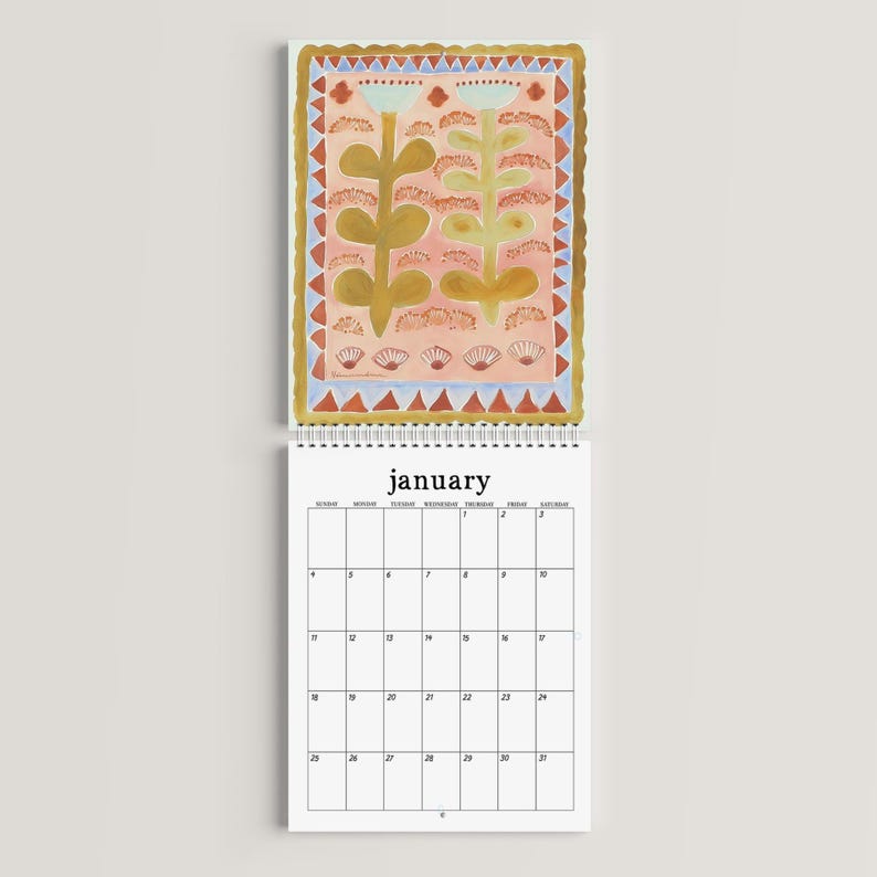 May include: A spiral-bound calendar open to January. The top portion features a colorful illustration of stylized flowers in shades of gold, pink, and blue, framed by a gold border. The calendar grid below is white with black text.