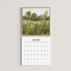 May include: A wall calendar featuring a landscape painting of a green field and trees at the top, with a white grid for the month of March below. The calendar has a brown and white checkered border and is bound by a white spiral wire.