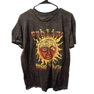May include: Dark gray t-shirt featuring the word "sublime" in yellow and orange above a sun graphic with a red face and blue eyes. Below the sun is the text "Long Beach" in a decorative font. The shirt has a crew neck and short sleeves.
