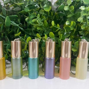 May include: Six small glass bottles with gold caps and a variety of colours, including yellow, green, blue, purple, pink, and light yellow. The bottles are hanging from a string.