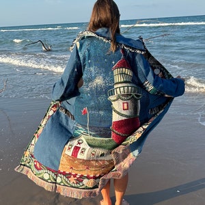 May include: A woman wearing a blue denim jacket with a tapestry design featuring a lighthouse, stars, and a house. The tapestry is fringed and has a colorful design.