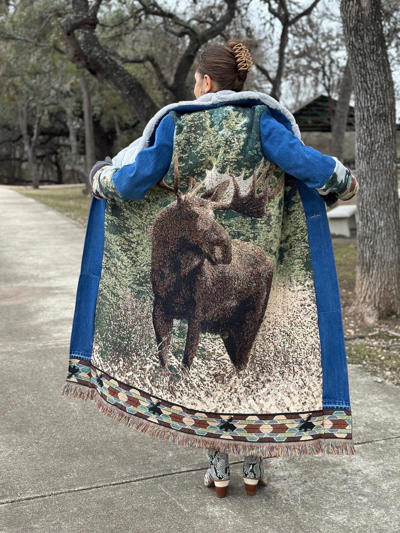 May include: A long denim jacket with a moose tapestry on the back. The jacket has a sherpa lining and a fringe trim.
