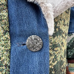 May include: Close-up of a denim jacket with a patterned fabric panel and a silver button with an ornate design.
