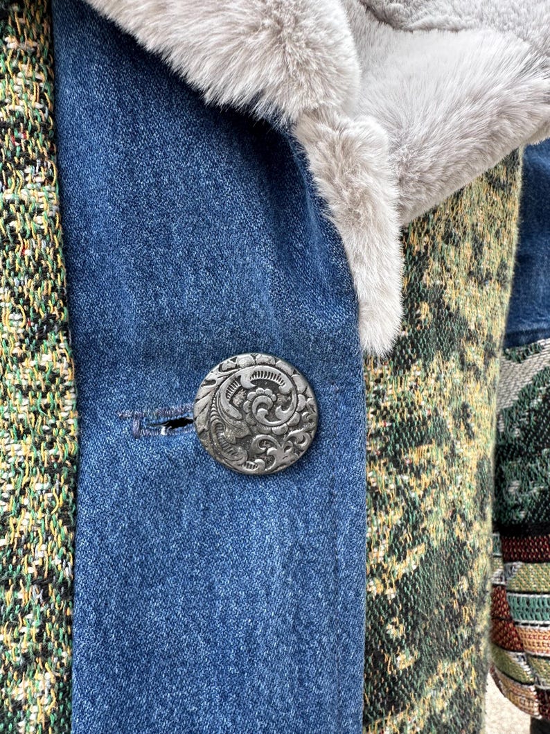 May include: Close-up of a denim jacket with a patterned fabric panel and a silver button with an ornate design.