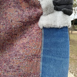 May include: Close-up of a jacket lining with a colorful woven fabric, a white faux fur trim, and a denim skirt.