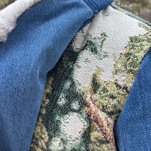 May include: A denim vest with a white faux fur collar and a tapestry-style back panel featuring a green, white, and gold floral design.