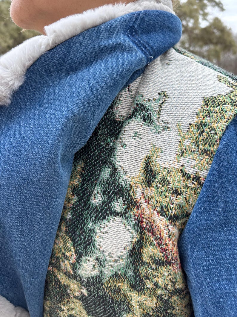 May include: A denim vest with a white faux fur collar and a tapestry-style back panel featuring a green, white, and gold floral design.
