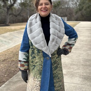 May include: A long blue denim coat with a faux fur collar and a green and brown patterned design. The coat has a button closure and a long sleeve.