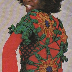 May include: A woman wearing a red top with a green, black, and yellow crocheted vest featuring a sunflower design.