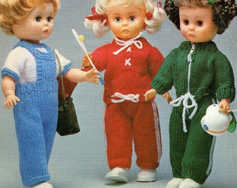 Op de afbeelding: Drie poppen met gebreide outfits. De pop links draagt een blauw en wit gebreid outfit. De pop in het midden draagt een rood gebreid outfit. De pop rechts draagt een groen gebreid outfit.