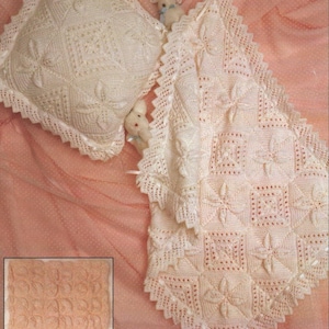 Puede incluir: Juego de manta y almohada de bebé de ganchillo color crema. La manta presenta un patrón floral y un borde festoneado. La almohada tiene forma cuadrada con un diseño floral a juego. Un pequeño juguete está colocado cerca de la manta.