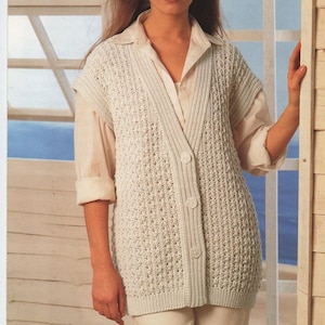 Può includere: Un gilet bianco senza maniche in maglia con chiusura a bottoni. Il gilet ha un delicato motivo traforato ed è indossato sopra una camicia bianca con bottoni.