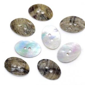 May include: A collection of seven oval-shaped buttons featuring two centre holes. Four buttons display a dark, mottled brown and grey pattern with a natural texture, while three buttons exhibit a smooth, iridescent white mother-of-pearl finish.